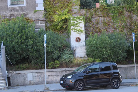 Monumento ai caduti di Sturla, circondato da vegetazione e un'auto parcheggiata sul lato della strada.
