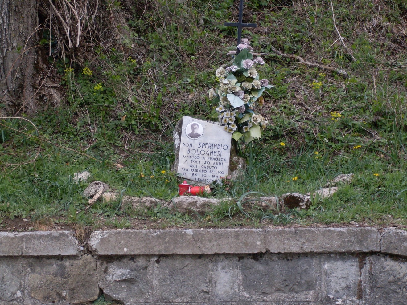 Cippo commemorativo a Bolognesi, con fiori e un piccolo monumento in memoria di un defunto.