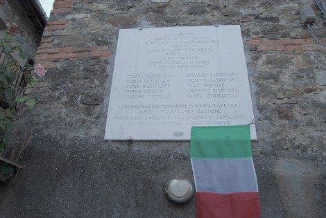 Lapide commemorativa che ricorda le vittime dei confini e della guerra. Bandiera italiana in evidenza.