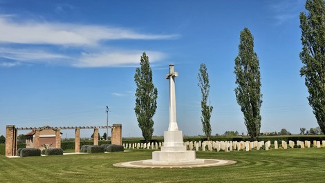 Cimitero militare "Argenta Gap" con croce centrale e alberi, circondato da tombe in un paesaggio sereno.