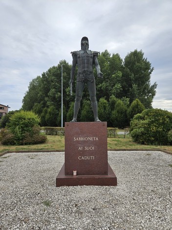 Monumento commemorativo ai caduti di Sabbioneta, con figura imponente e base in marmo. Giardini curati circostanti.