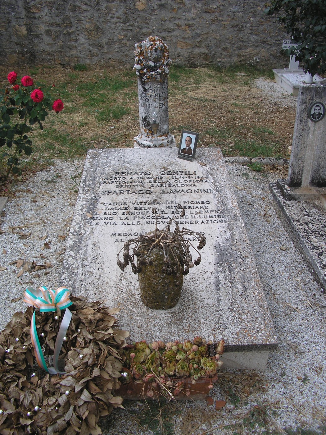 Sepolcro di Gentili, con lapide e decorazioni floreali, situato in un cimitero. Atmosfera di memoria e rispetto.