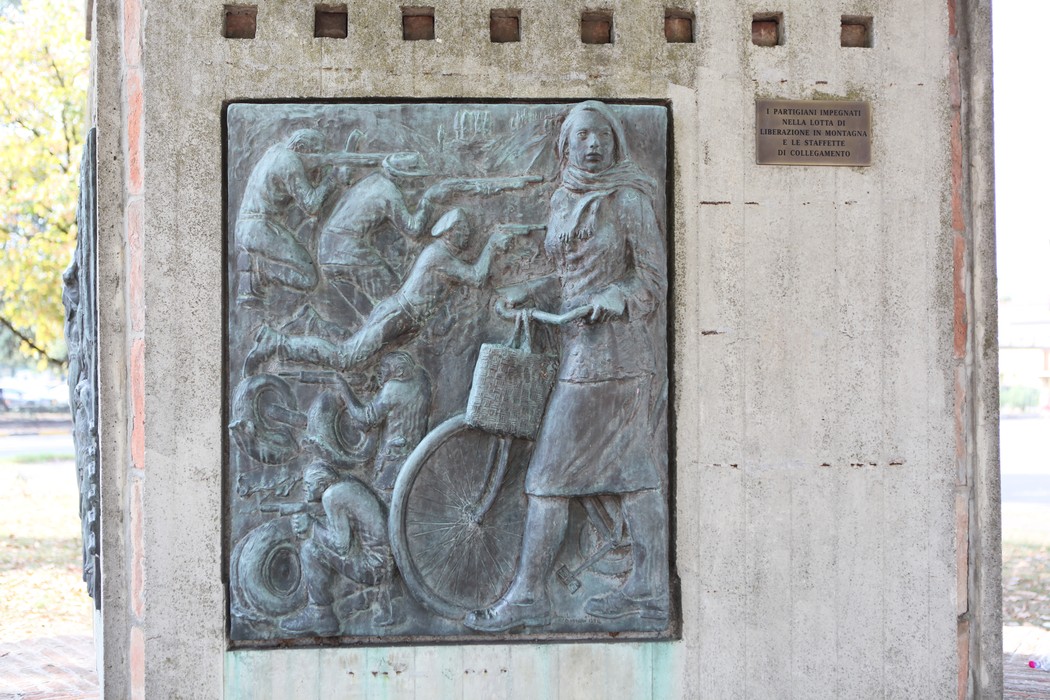 Monumento alla Resistenza con bassorilievo di figura femminile in bicicletta e scene di lotta.