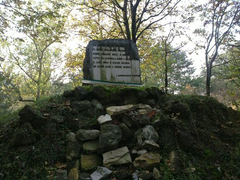 Cippo commemorativo a Meglioli immerso nella natura, circondato da alberi e roccia.