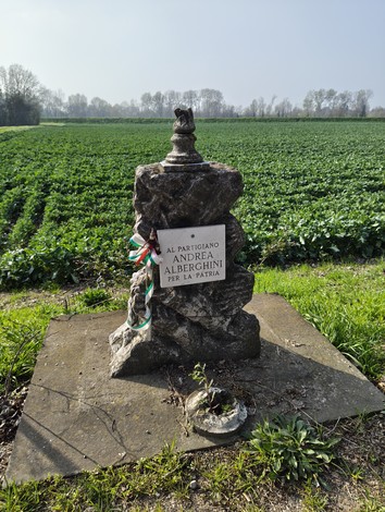 Cippo commemorativo ad Alberghini dedicato ad Andrea Alberghini, circondato da un campo verde.