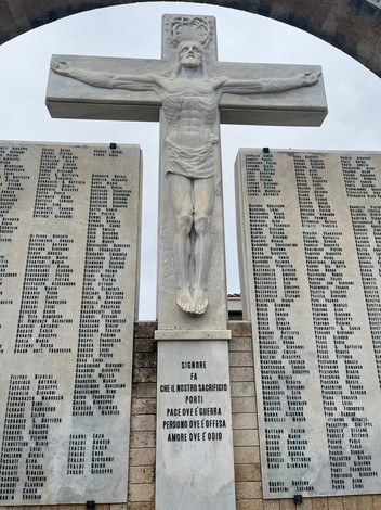 Statua di Cristo crocifisso con dipinti commemorativi e iscrizioni, simbolo di memoria e pace.