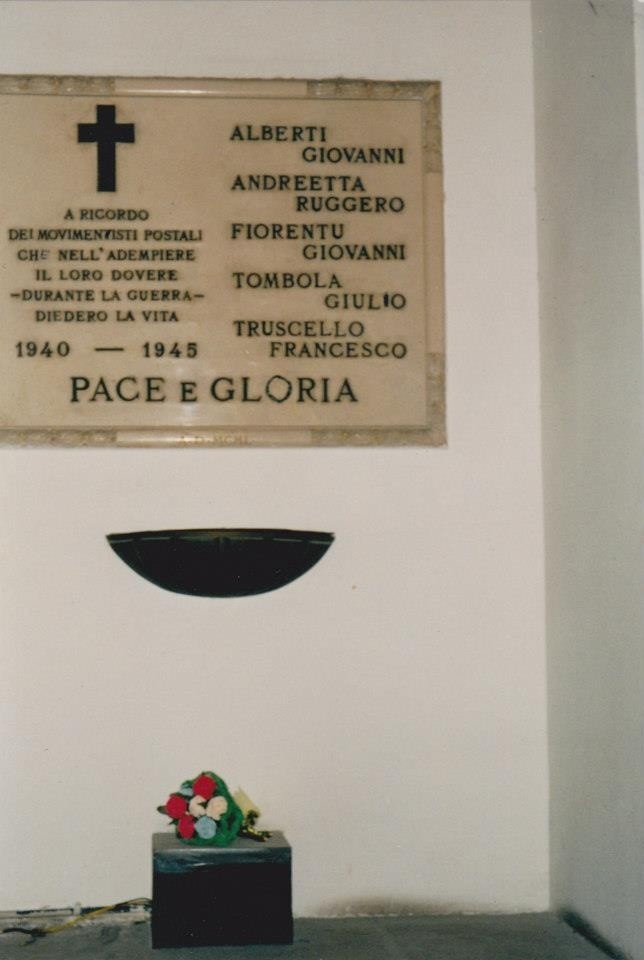 Lapide commemorativa in onore dei postali caduti, con una corona di fiori ai piedi e scritte in memoria.