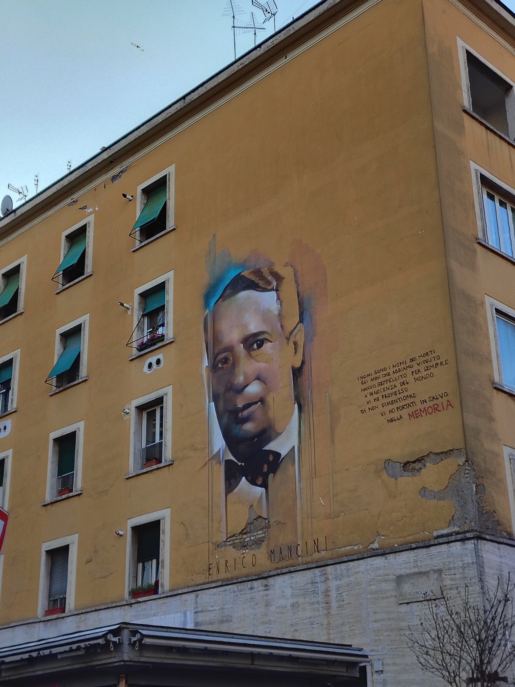 Murale che ritrae un uomo con cravatta, su una parete gialla di un edificio a Mancini.