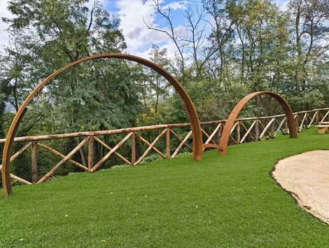 Percorso per Fornasini: vista su un sentiero con archi in legno e prato verde, immerso nella natura.