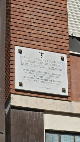 Lapide commemorativa dedicata a Don Giovanni Minzoni, situata su un muro in un contesto urbano.