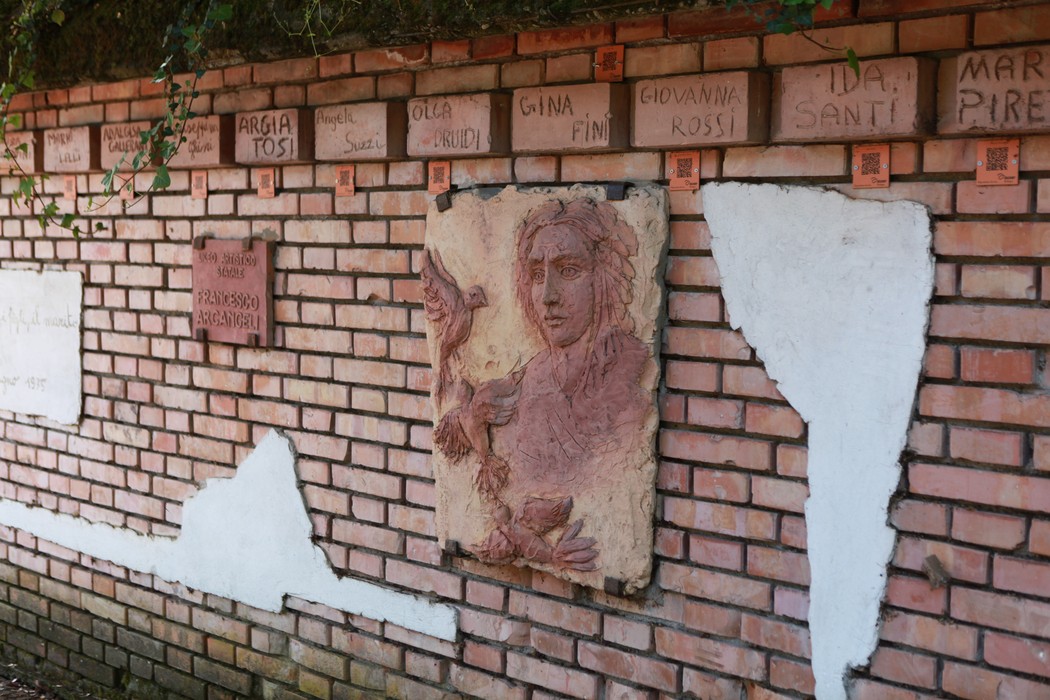 Monumento delle 128 partigiane, con rilievi e mattonelle commemorative su una parete di mattoni.