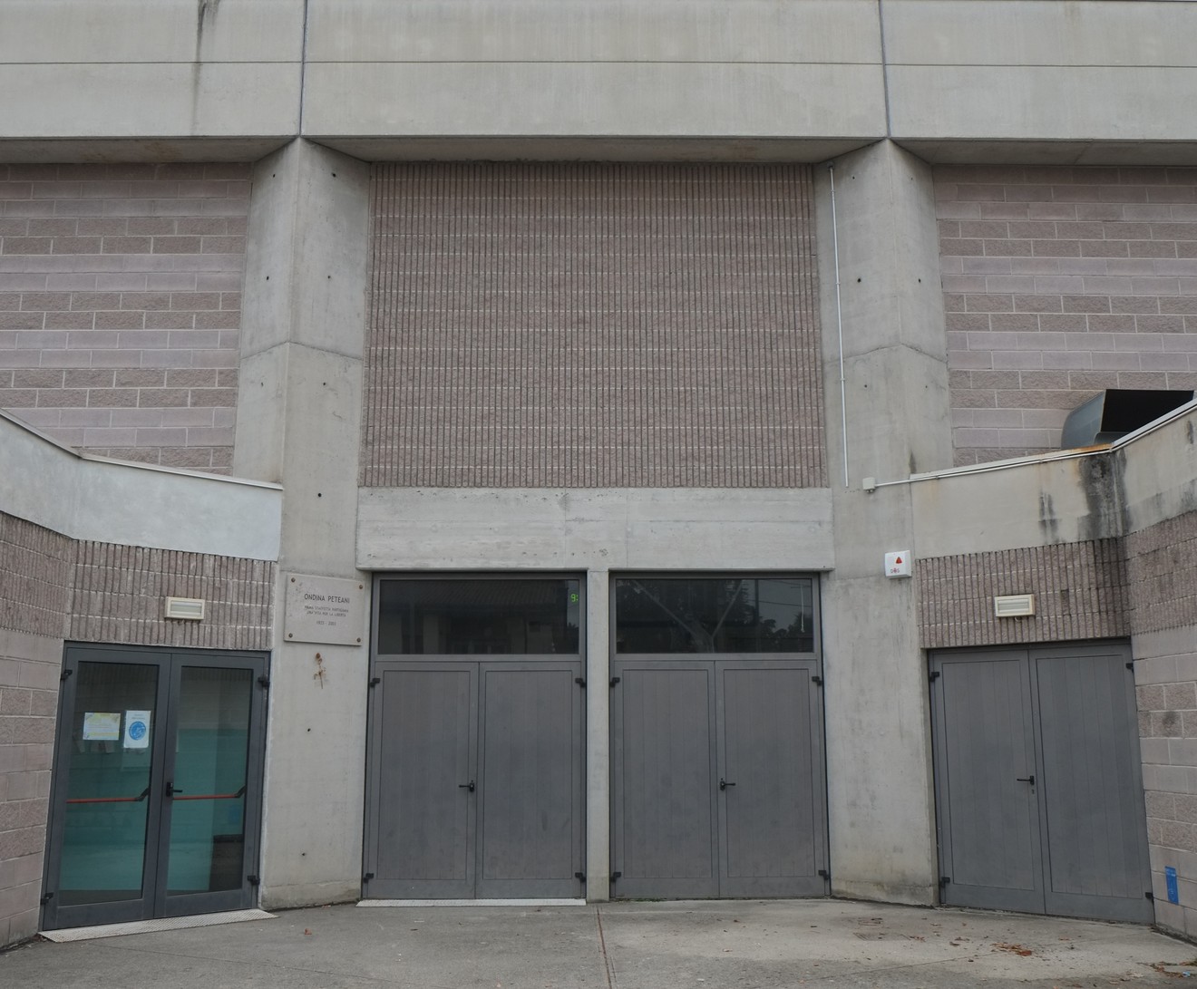 Lapide a Peteani, ubicata su un edificio moderno con ingresso in metallo e mattoni a vista.