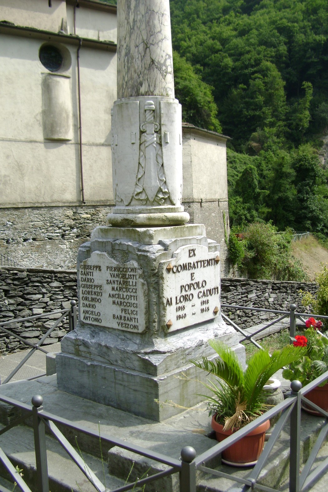 Monumento ai caduti di Cardoso, memoriale in pietra con nomi di soldati, circondato da vegetazione e fiori.
