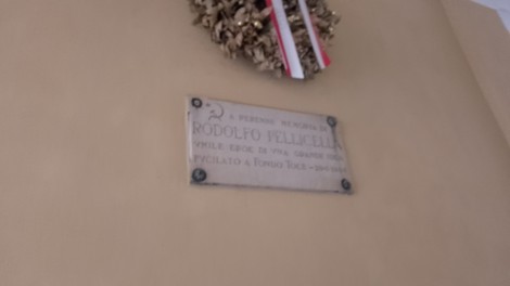 Lapide commemorativa dedicata a Rodolfo Pellicella, situata su una parete con una corona di fiori.