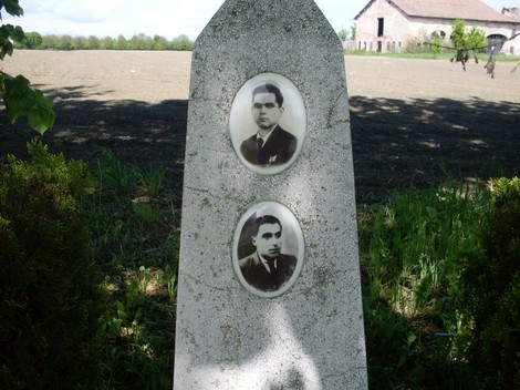 Cippo commemorativo con ritratti di Ferretti e Severi, situato in un paesaggio rurale.