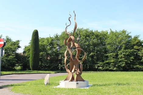 Monumento moderno con forme sinuose, situato in un'area verde, circondato da alberi e strade.