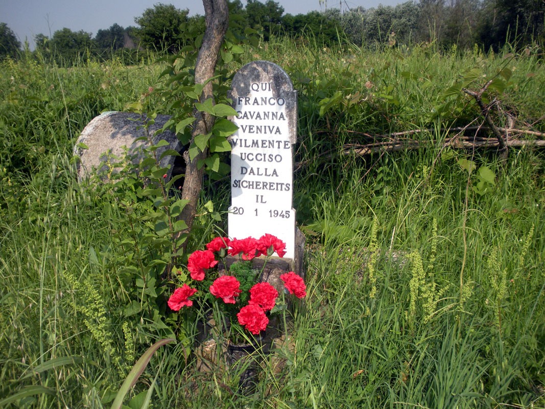 Cippo commemorativo a Cavanna, dedicato a Franco, vittima della guerra, circondato da erba e fiori.