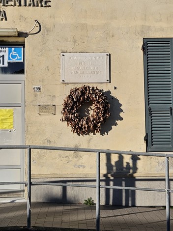 Lapide commemorativa dedicata ai caduti per la libertà a Pitelli, con corona di foglie secche.