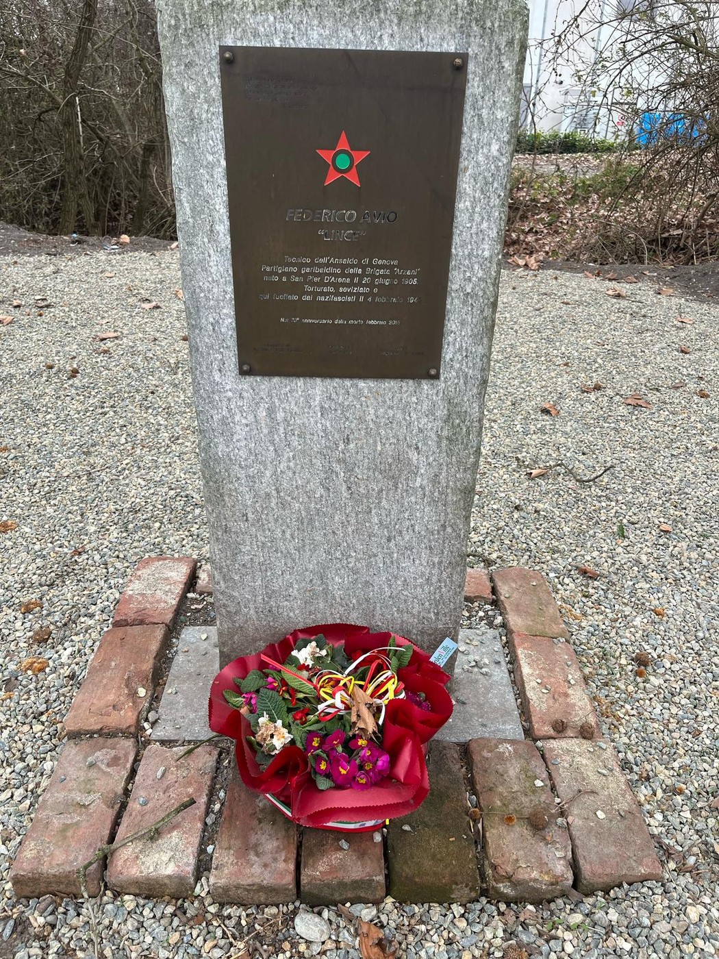 Monumento dedicato a Avio, con una pietra grigia e un omaggio floreale ai piedi.