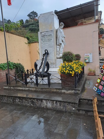 Monumento ai caduti di Strettoia, con statue e decorazioni floreali, in un contesto urbano.