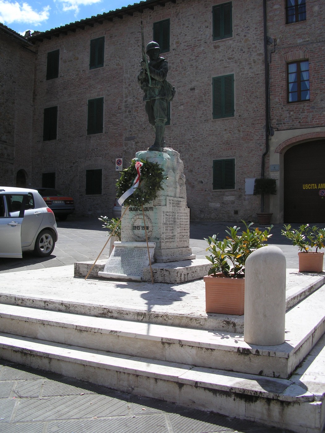 Monumento ai caduti con statue e una corona, situato in un contesto storico e urbano.