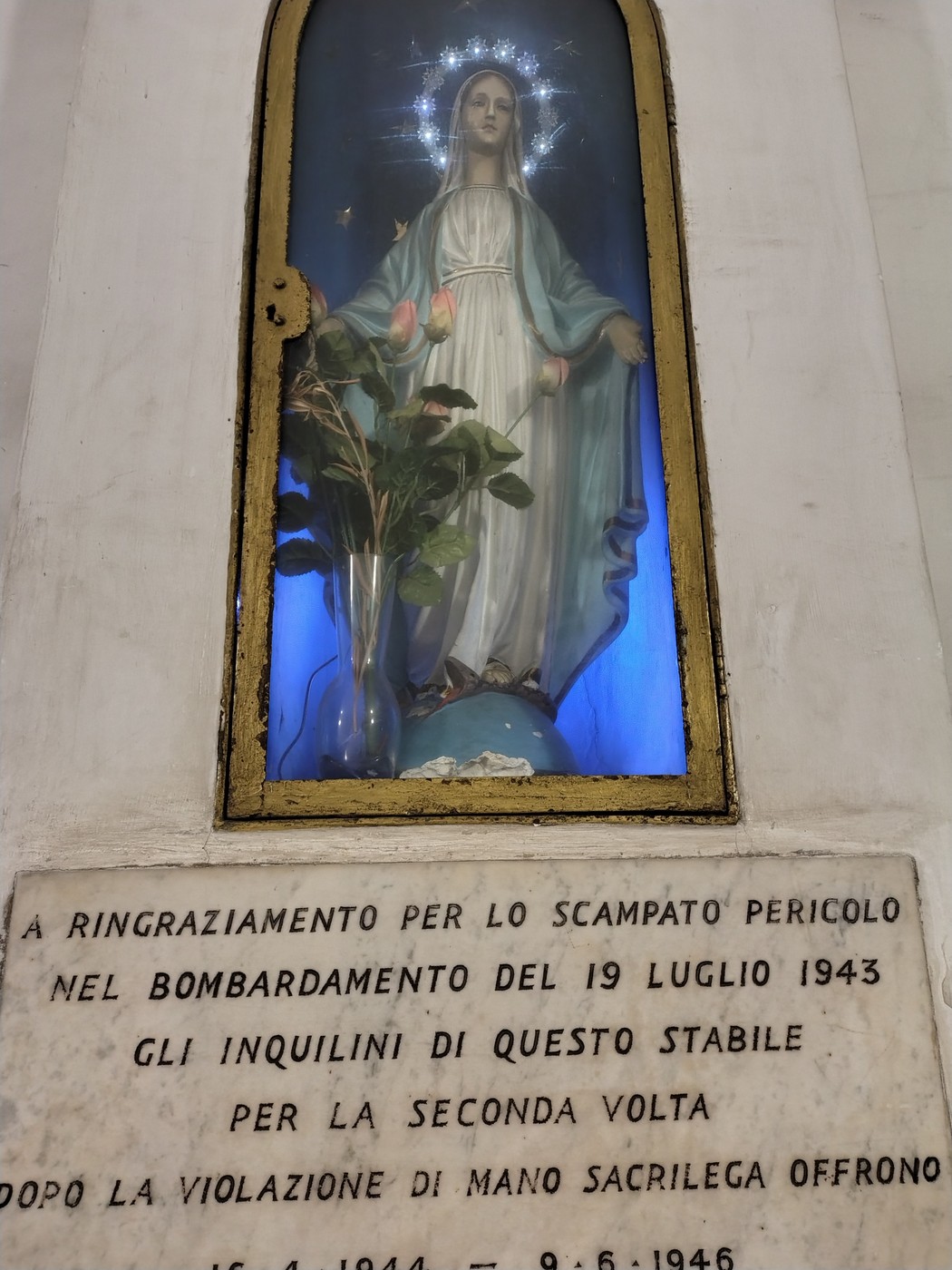 Statua della Madonna, illuminata, con dedica al bombardamento del 19 luglio 1943 e un ramoscello di rosa.