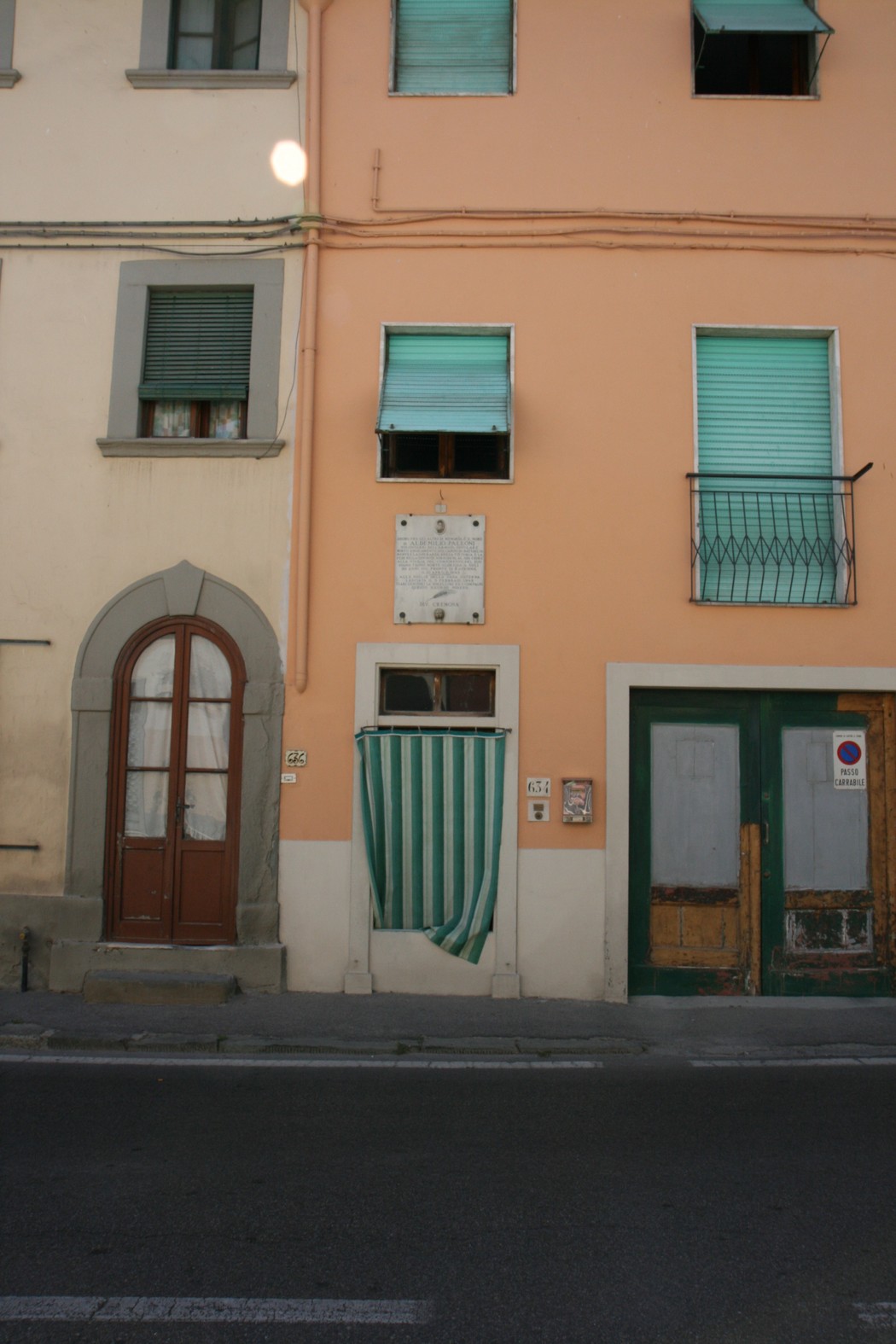 Lapide commemorativa "Lapide a Palloni" su un edificio con finestre verdi e porta in legno.
