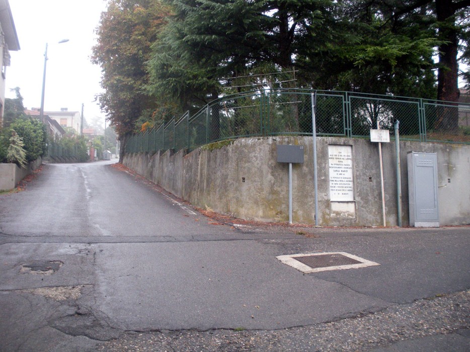 Strada con lapide a Sanga, immersa nel verde e nel mistero di una mattina nebbiosa.
