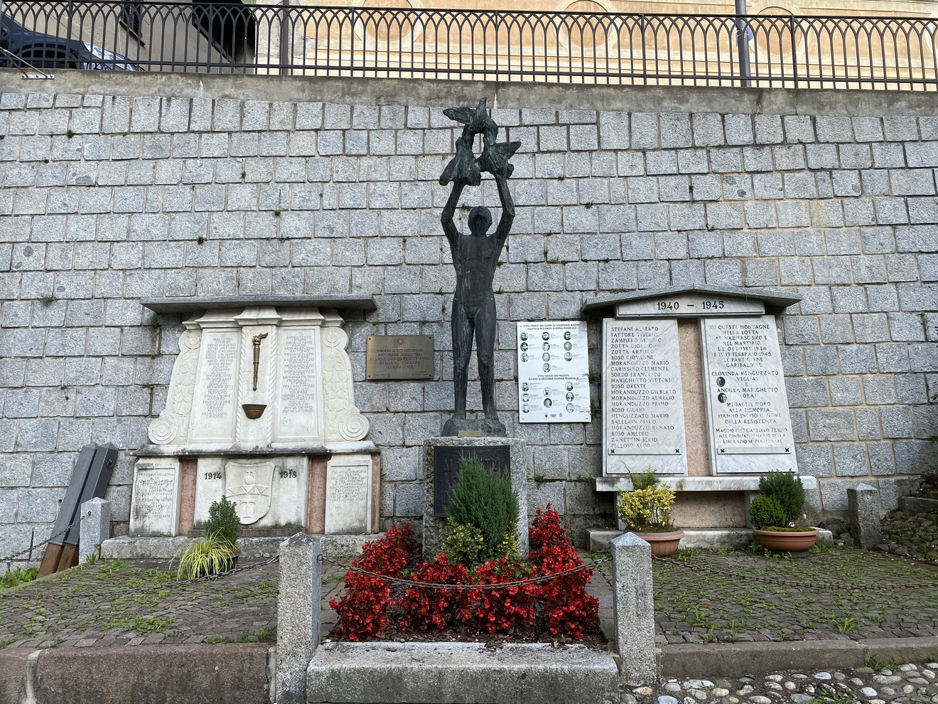 Monumento ai caduti di Castello Tesino, con statue e lapidi commemorative circondate da fiori.