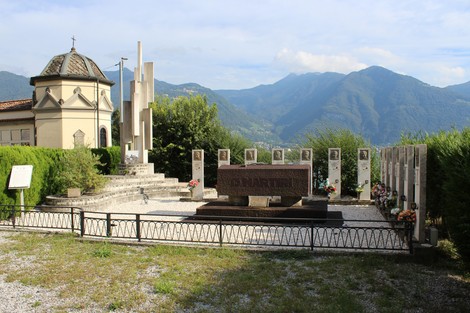 Monumento commemorativo "Sacrario dei Tredici Martiri" immerso nel verde, con montagne sullo sfondo.