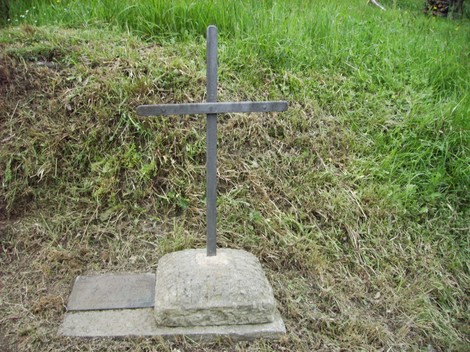 Cippo di Bertocci: croce di metallo su base di pietra, circondata da erba verde.