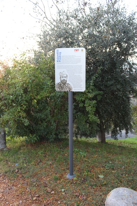 Targa informativa su Predrag, con illustrazione e testo descrittivo in un contesto di verde urbano.