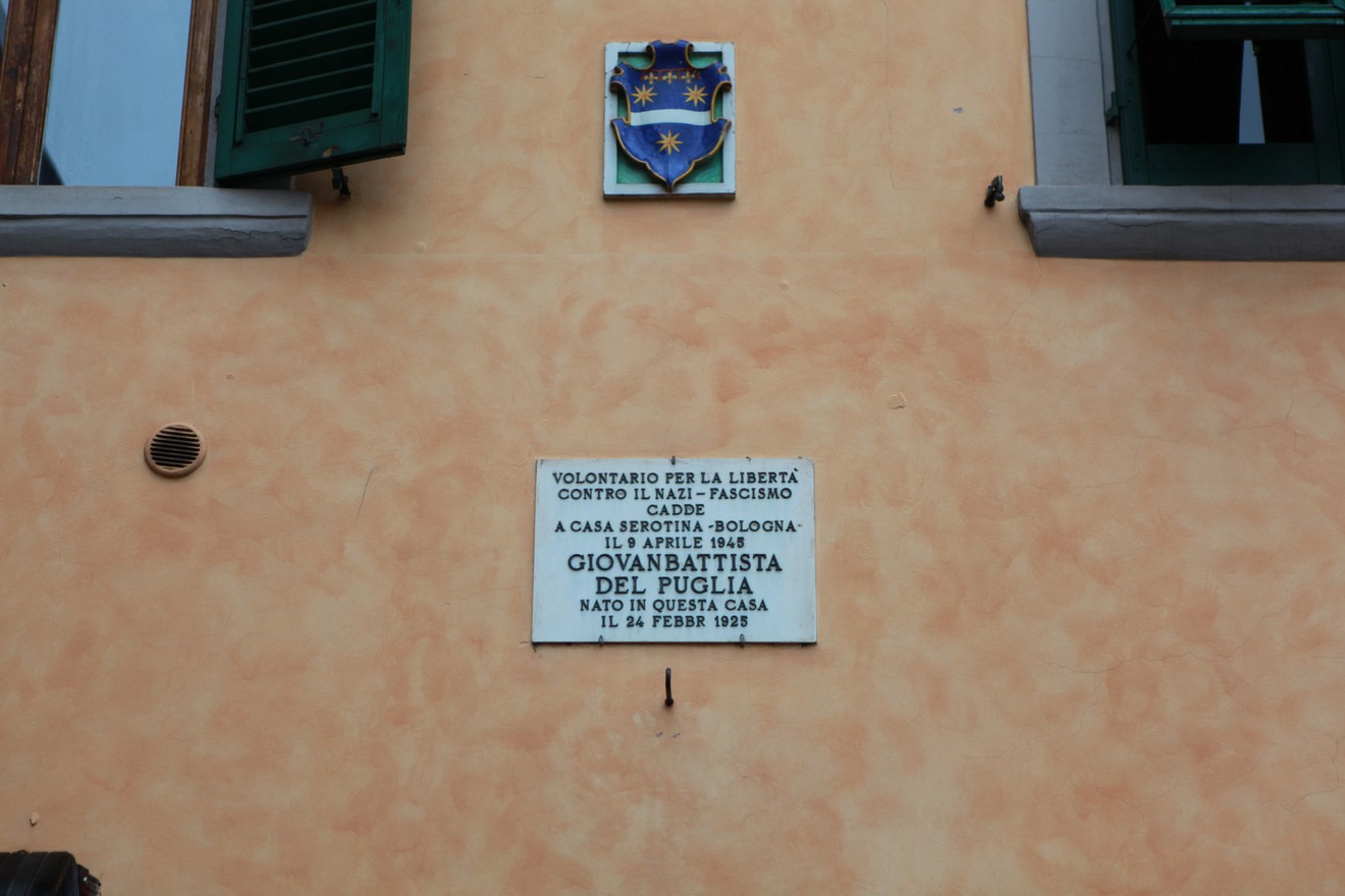 Lapide commemorativa dedicata a Giovan Battista del Puglia, situata su un edificio storico.