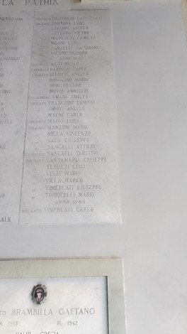 Cappella ai caduti di Brugherio con nomi dei soldati onorati su una targa in metallo. Atmosfera di ricordo e rispetto.