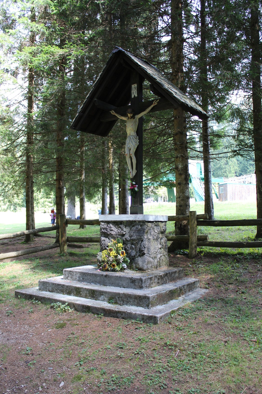 Crocifisso dei Partigiani, monumento situato in un'area verde circondata da alberi, con fiori ai piedi.