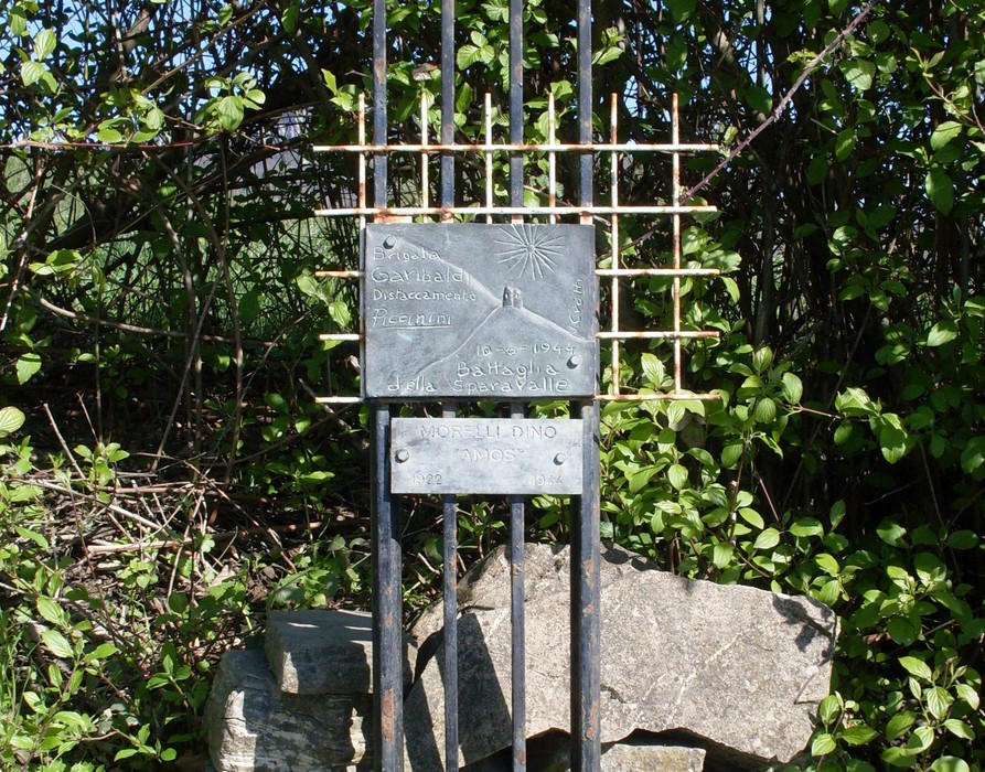 Monumento a Morelli, commemorativo, con elementi decorativi e incisioni su metallo tra vegetazione.