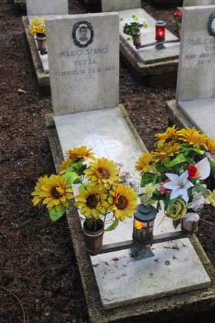 Tombe con fiori e candele in un luogo dedicato ai caduti per la Libertà.