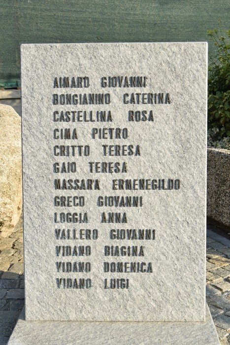 Monumento in pietra con elenco di nomi incisi, collocato all'aperto su pavimentazione in ciottoli.