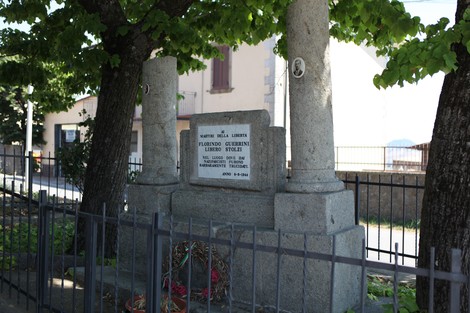 Il Monumento a Guerrini e Stolzi è sormontato da colonne e circondato da alberi, con una base in pietra.