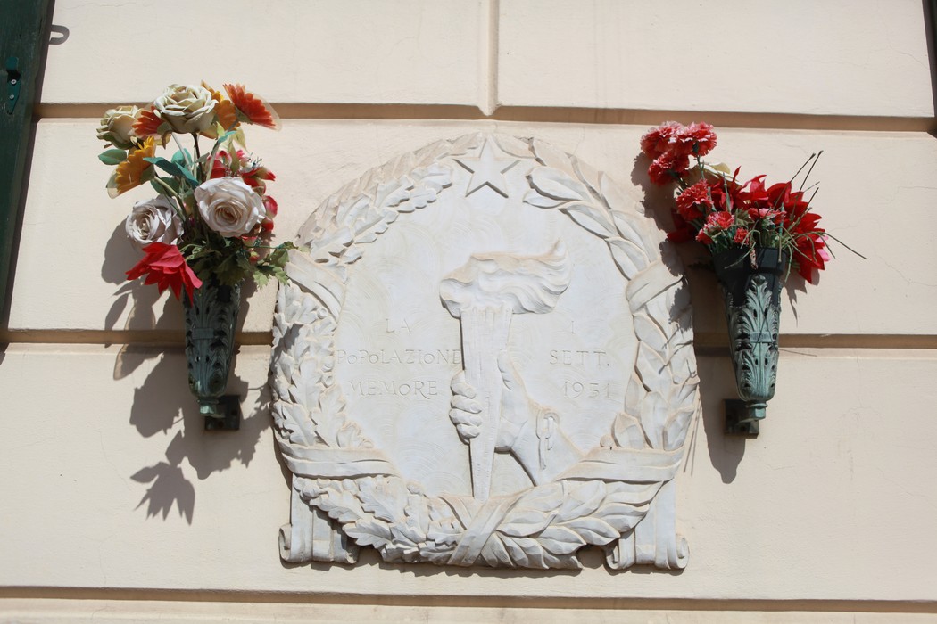 Lapide commemorativa dedicata ai caduti per la Libertà, decorata con fiori artificiali.