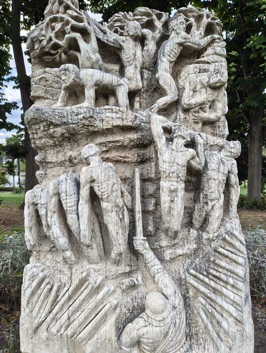 Monumento in pietra scolpita, con figure umane in rilievo, collocato in un'area alberata.
