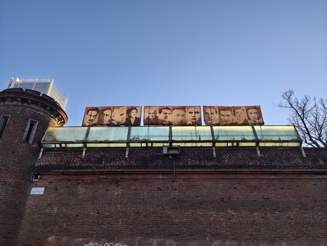 Pannelli artistici sui volti degli imprigionati all'esterno del carcere Le Nuove, sotto un cielo blu.