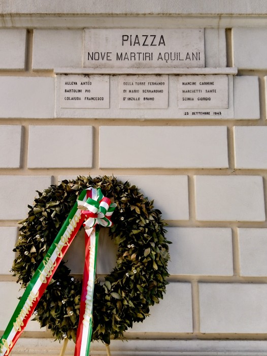 Lapidi commemorative dedicate ai nove martiri aquilani, con una corona di alloro e nastro tricolore.