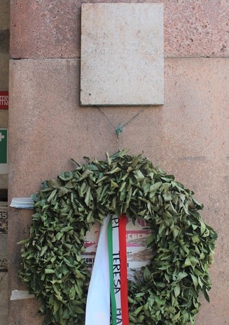 Lapide commemorativa con corona di alloro, situata su una parete in pietra.