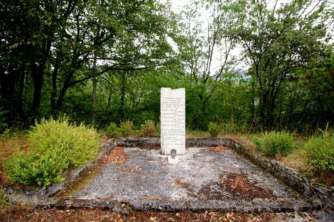 Cippo commemorativo in memoria dei partigiani uccisi a Colle di Postignano, immerso nella natura.