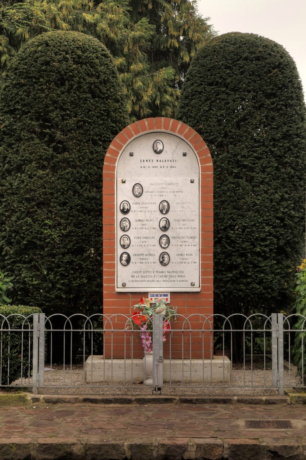 Monumento commemorativo ai caduti per la libertà a Budrione, con nomi incisi e decorazioni floreali.
