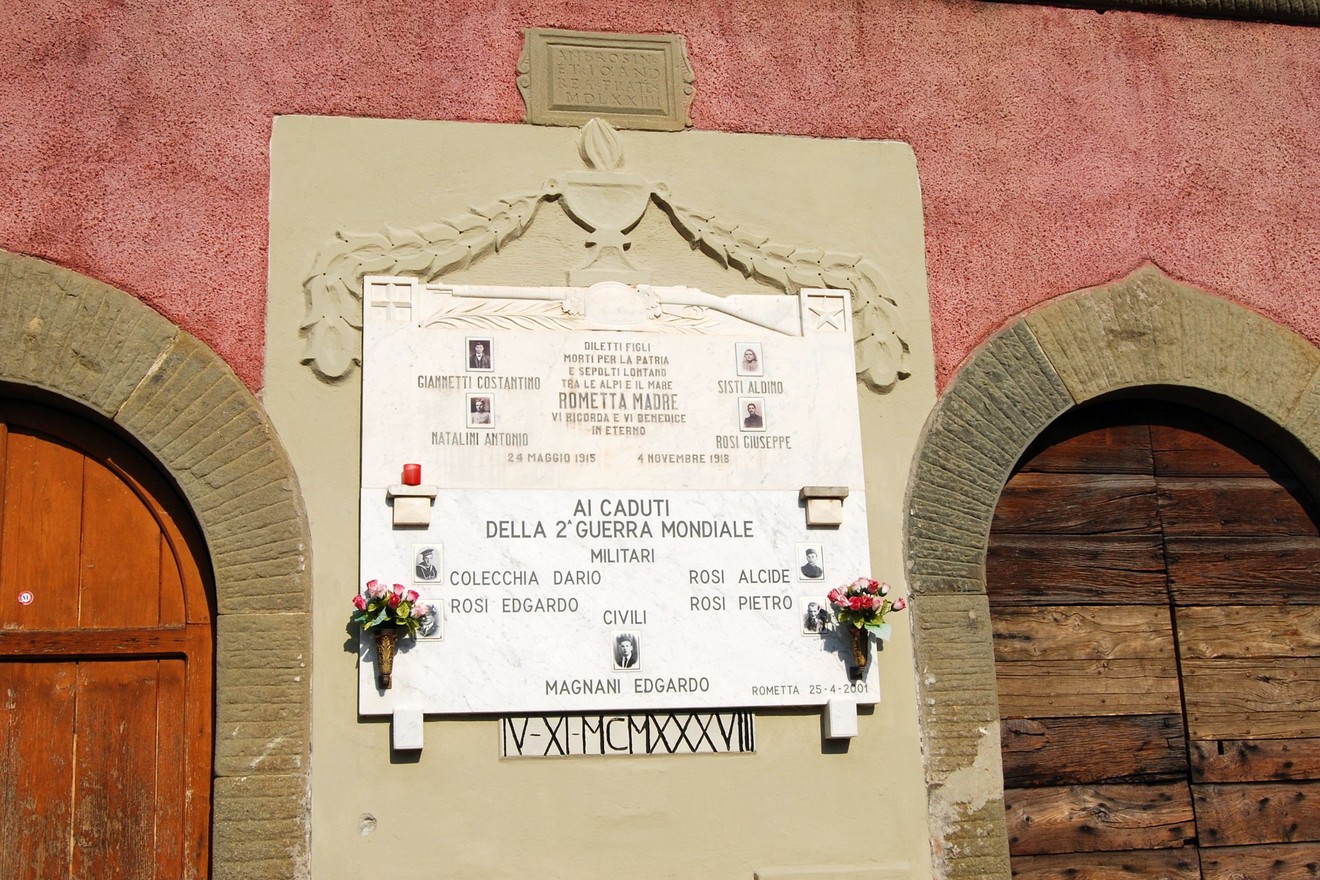 Lapide commemorativa ai caduti della Seconda Guerra Mondiale a Rometta, decorata con fiori e incisi ricordi.