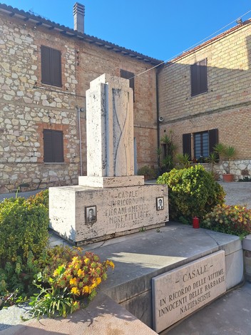 Monumento commemorativo dedicato a Fiorani e Moretti, con decorazioni floreali e un paesaggio architettonico circostante.