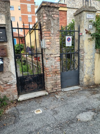 Porte in ferro battuto con muro di pietra, ingresso a un giardino privato ben curato.