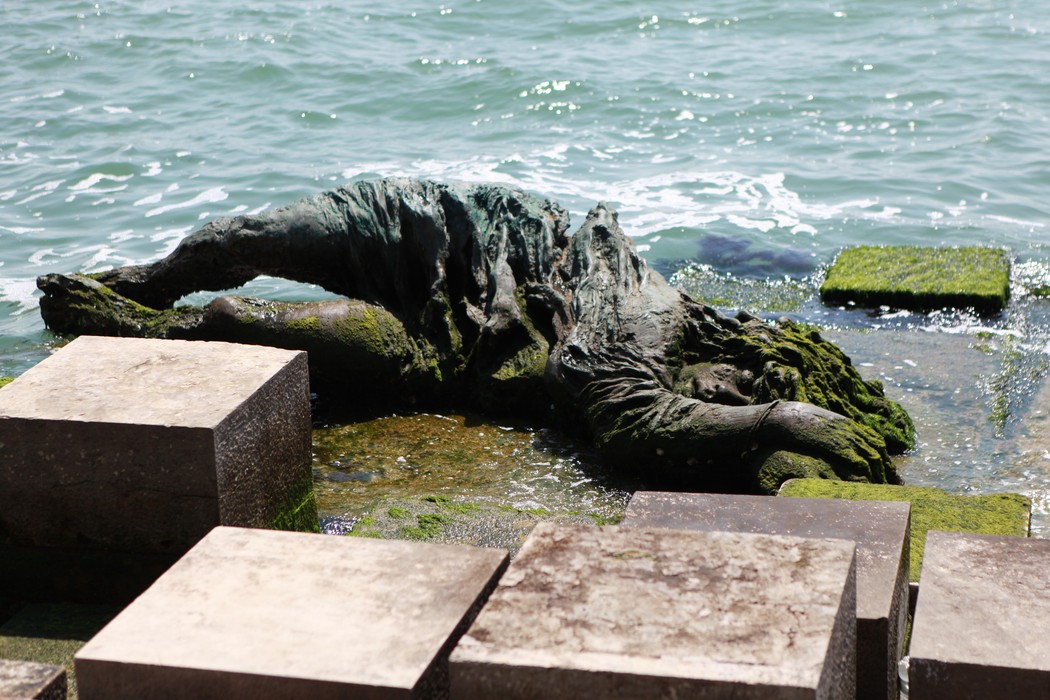 Monumento alla partigiana, scultura in bronzo che rappresenta una figura distesa vicino all'acqua, circondata da blocchi di pietra.